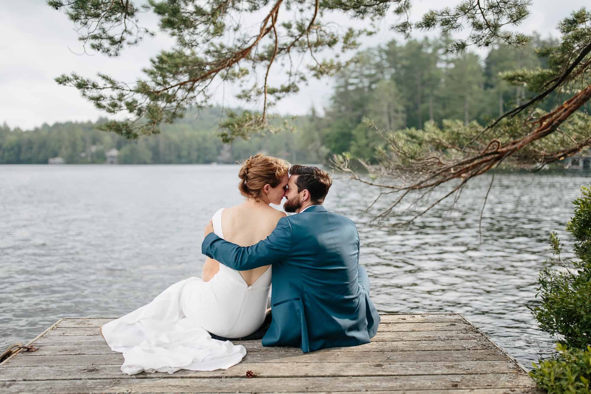 Bride and groom sit on dock on Upper Saint Regis - Adirondack Wedding Photography