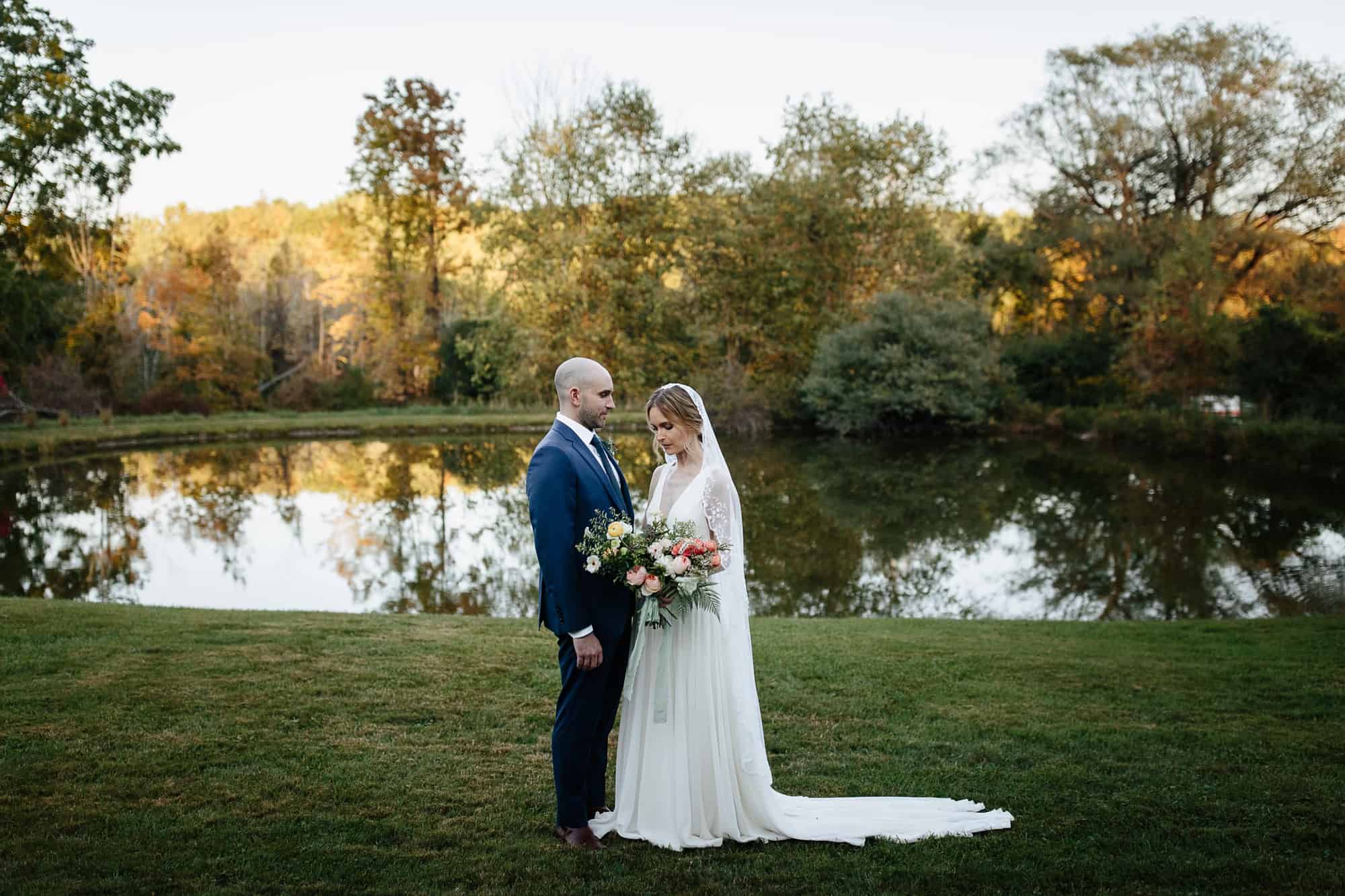 Bride and groom standing near pond at their M&D farm wedding in the Catskills capture by upstate New York wedding photographers The Light and Color