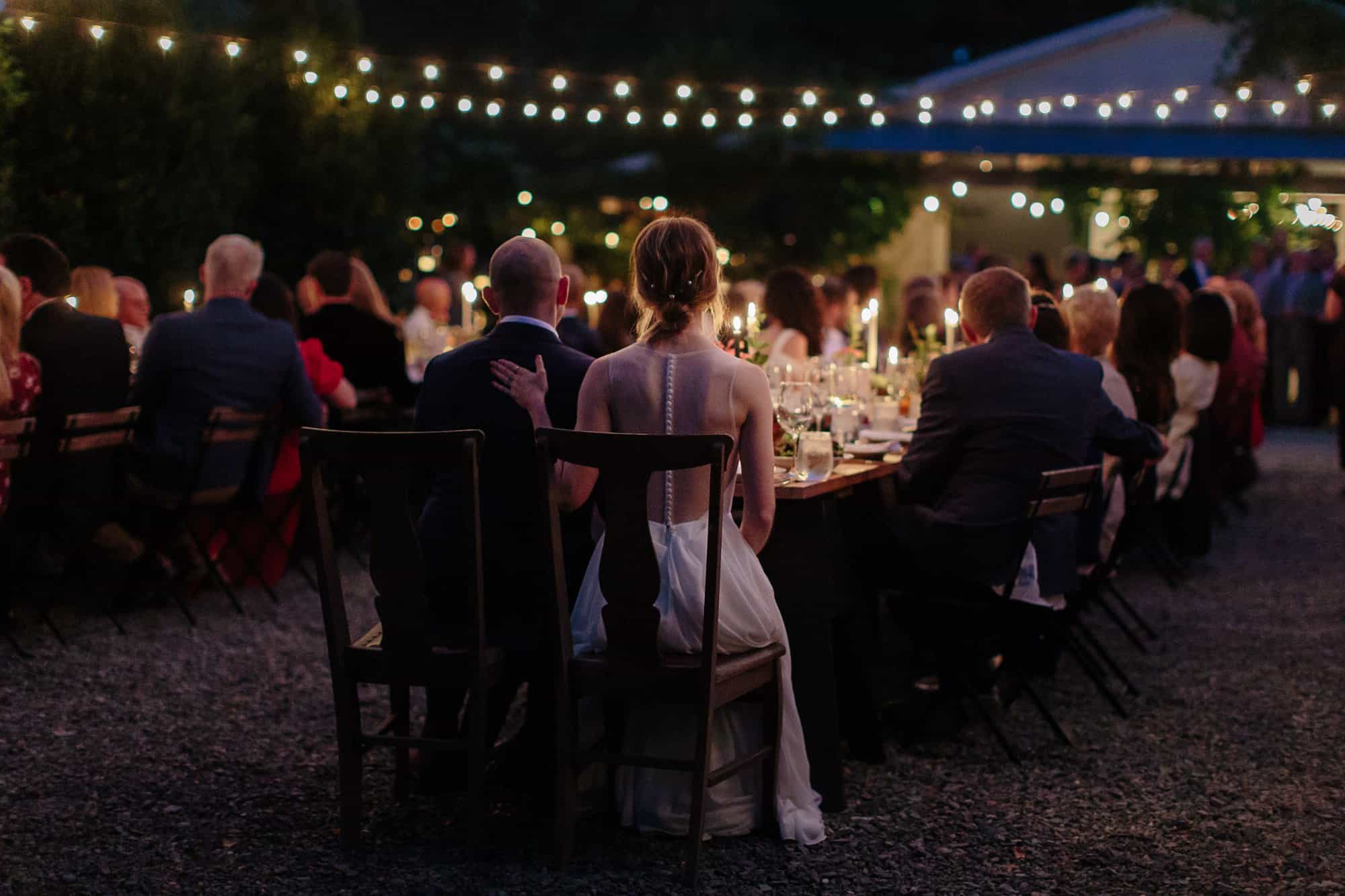 Bride and groom watching guests enjoying dinner at M&D farm wedding capture by Upstate new york wedding photographers The Light and Color
