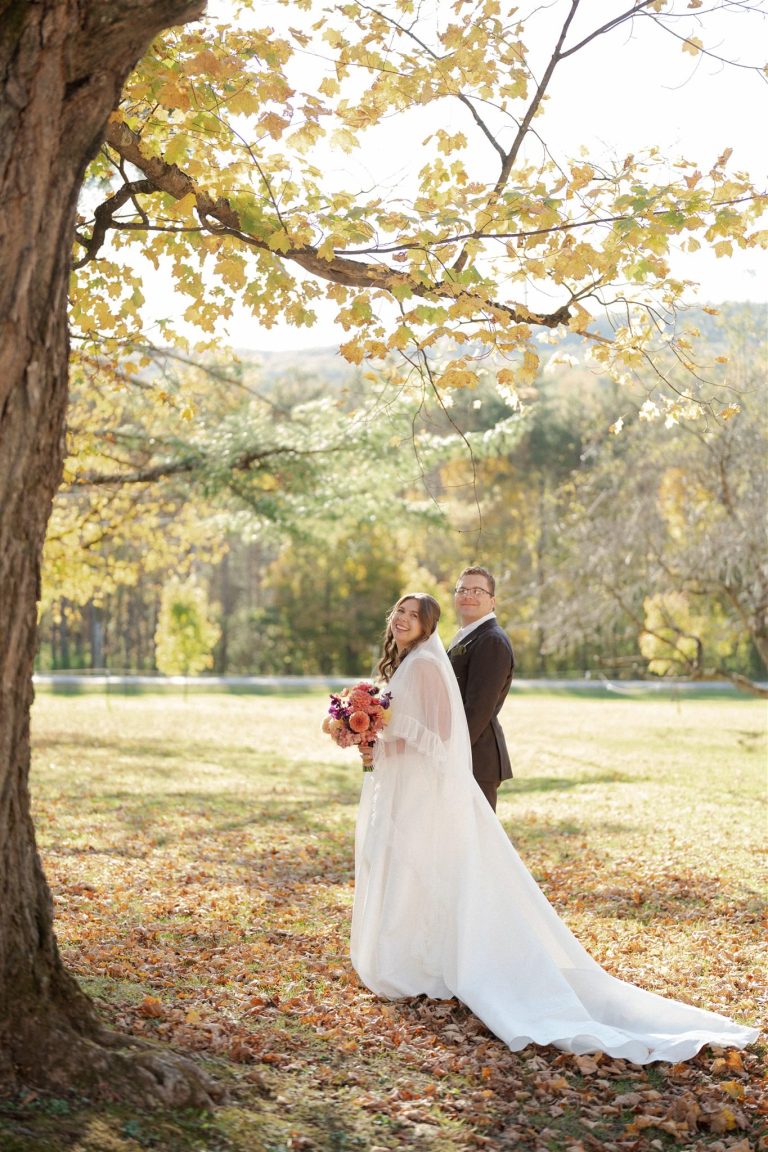 Bride and groom smiling under golden autumn tree; bride in white gown holding bouquet at The Tillerman wedding.